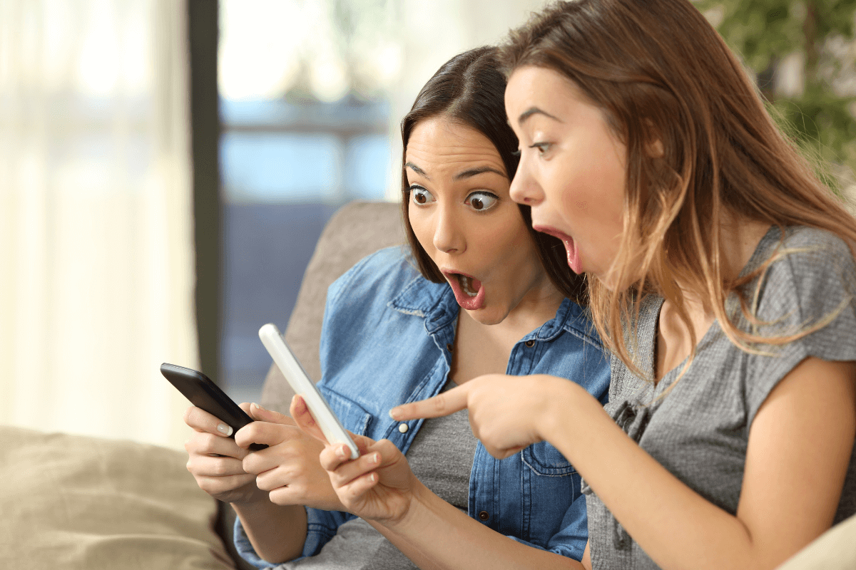 Duas mulheres com expressão de choque e surpresa olhando para a tela do celular, ilustrando a reação ao ver o preço de um conteúdo adulto exclusivo.