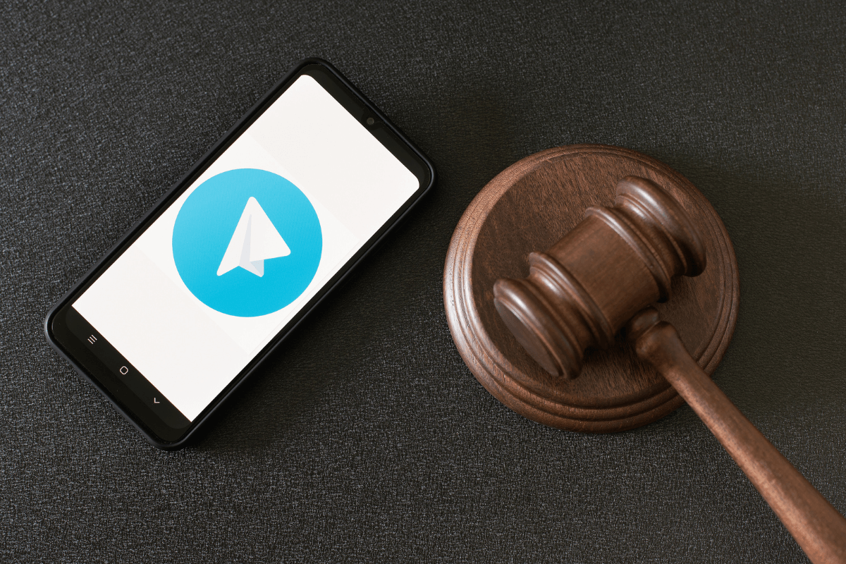 Celular com logo do Telegram ao lado de um martelo de juiz, representando os riscos legais e crimes no submundo dos grupos de conteúdo adulto