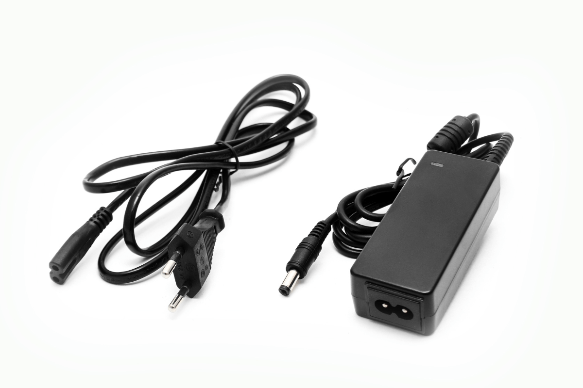 Carregador original e cabo de força para pistola massageadora Fonte de alimentação e cabo de força de uma pistola massageadora, mostrando o adaptador do tipo tijolinho e o conector de pino redondo (DC).