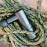 Pistola massageadora preta profissional sobre cordas de escalada, ilustrando o guia completo sobre como carregar a bateria corretamente.