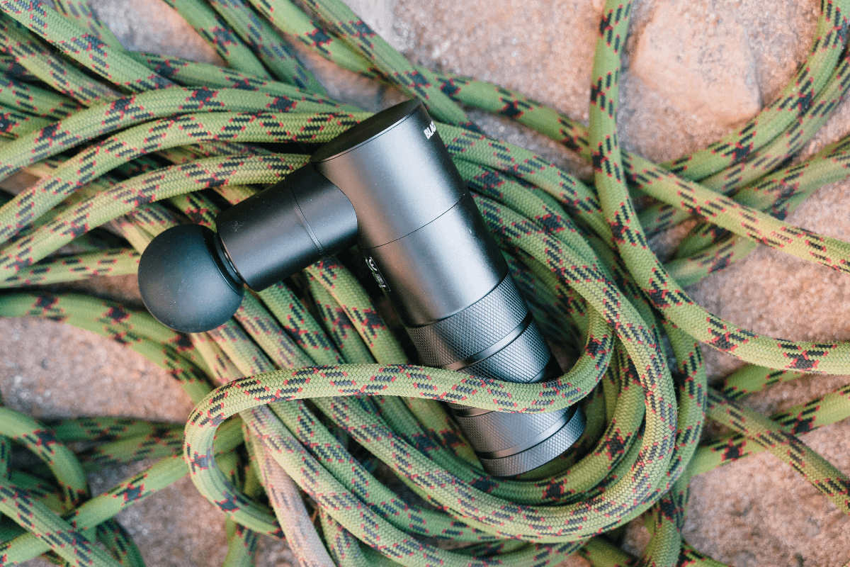 Pistola massageadora preta profissional sobre cordas de escalada, ilustrando o guia completo sobre como carregar a bateria corretamente.