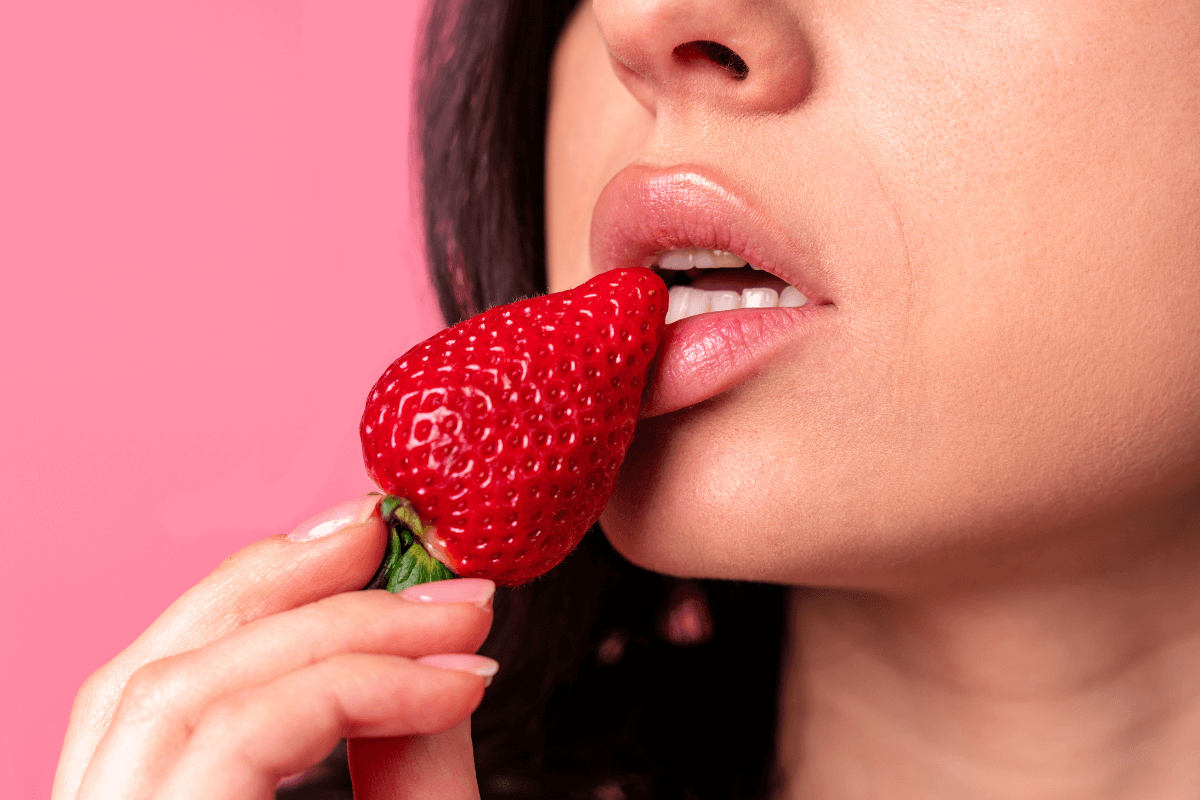Close sensual de mulher mordendo um morango, ilustrando estratégias profissionais sobre como posso ganhar dinheiro com conteúdo adulto.
