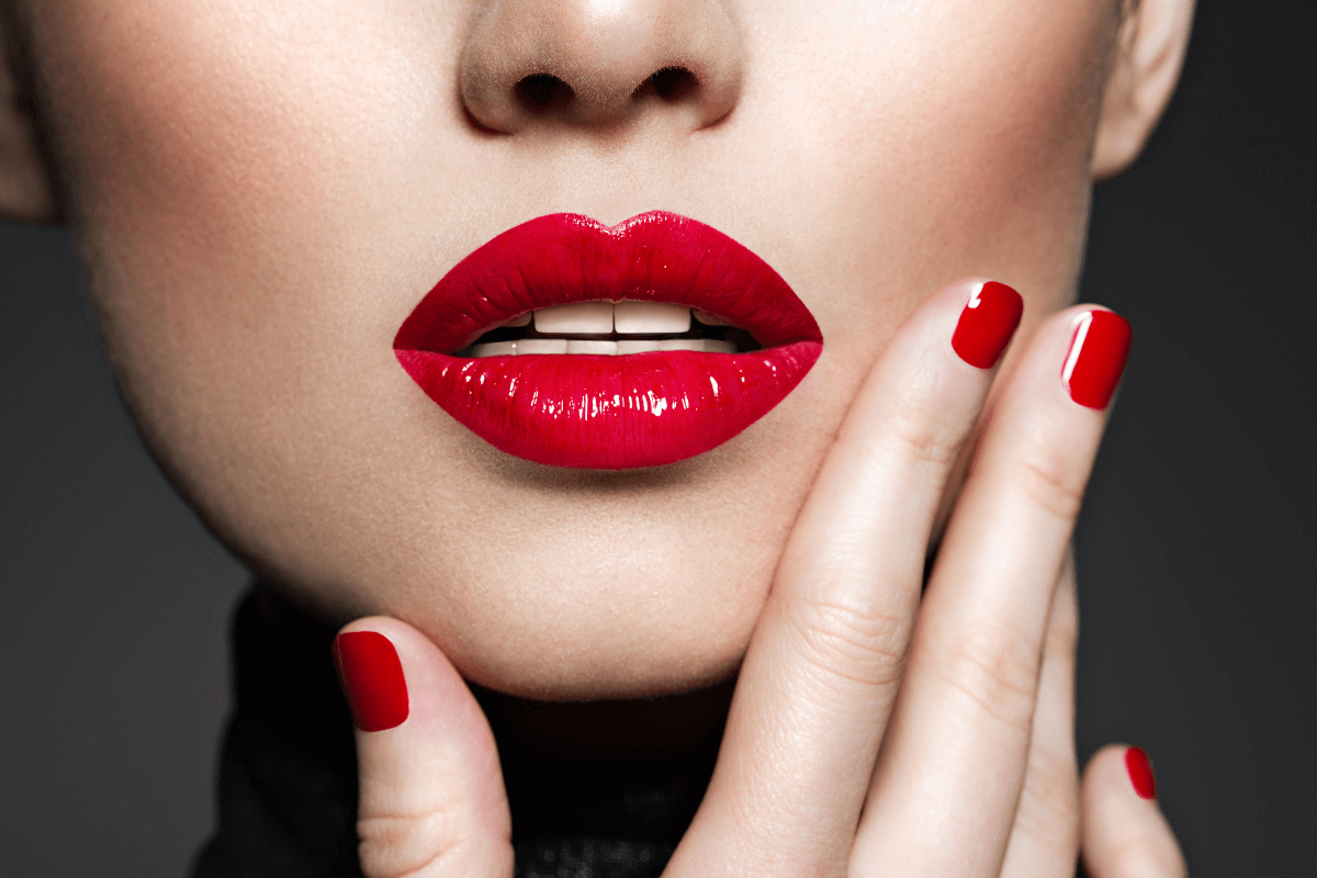 Close sensual de lábios com batom vermelho intenso e unhas pintadas, ilustrando a estética de marketing visual necessária para autores que buscam rentabilizar com contos eróticos no mercado digital.