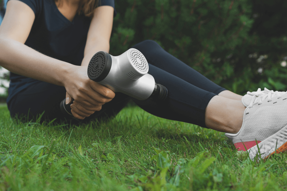 Aplicação segura evitando áreas de risco Mulher sentada aplicando a pistola massageadora na panturrilha com atenção, observando a pele para evitar áreas lesionadas ou proibidas.