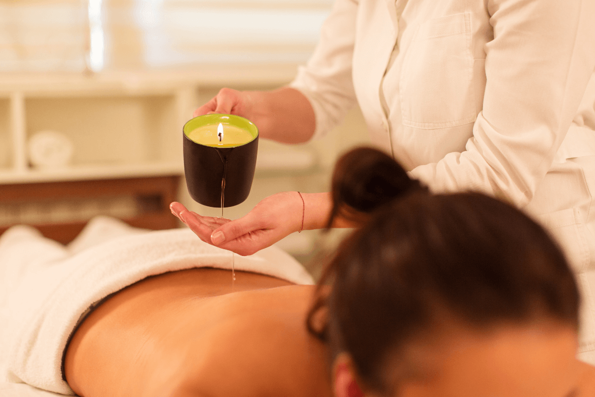 Terapeuta aplicando técnica segura de massagem com vela derramando o óleo na mão primeiro, ilustrando a diferença entre terapia relaxante e jogos de temperatura intensos.