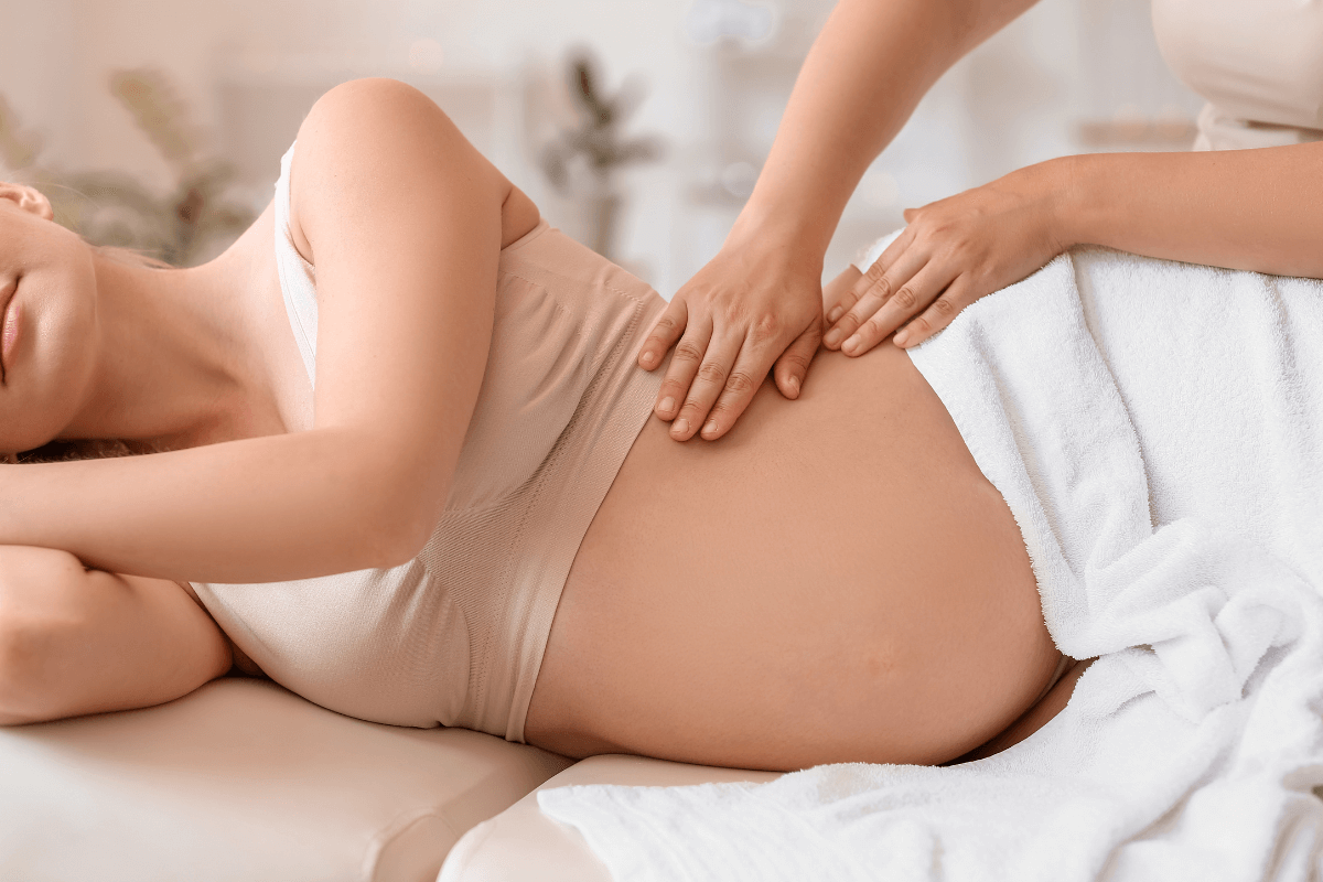 Terapeuta aplicando massagem manual suave em gestante deitada de lado, ilustrando a alternativa segura, já que a bambuterapia é proibida devido aos riscos de pressão no útero.