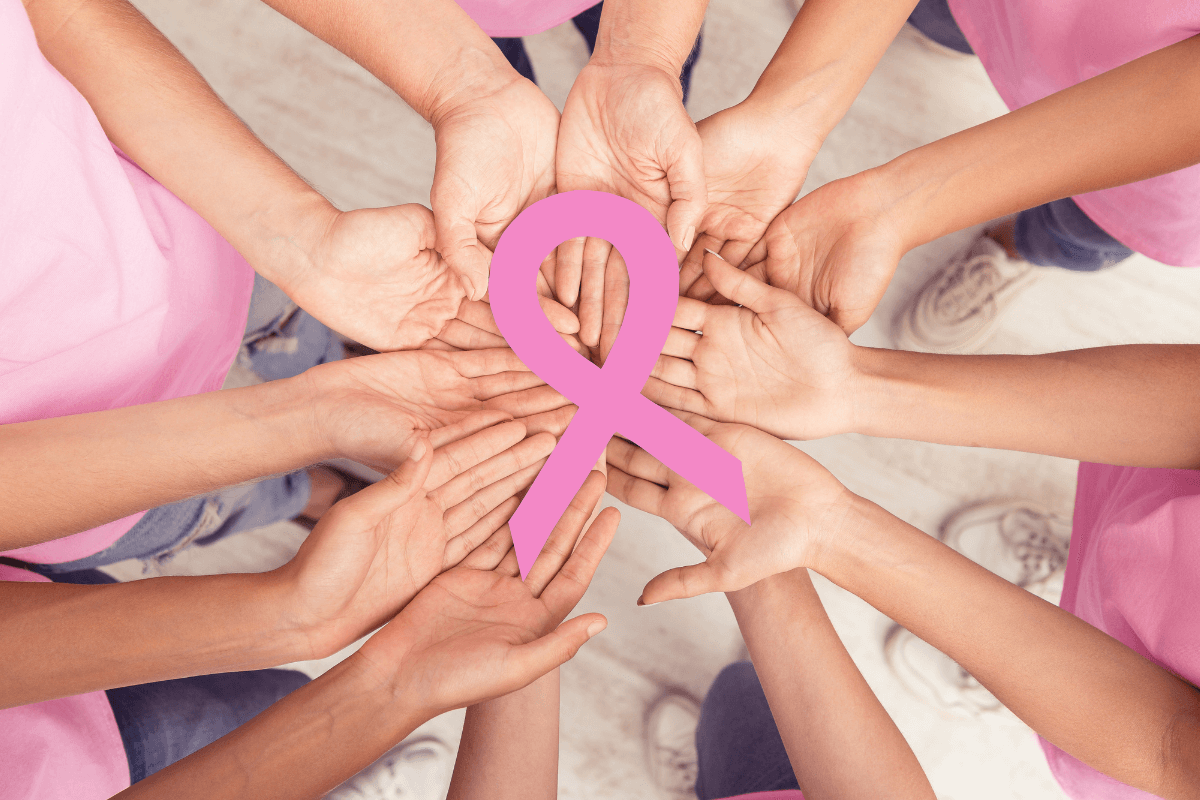 Mãos unidas segurando o laço rosa, ilustrando a seção de cuidados especiais e contraindicações do uso de massageador elétrico em pacientes com câncer e histórico oncológico, especialmente em áreas de radioterapia.