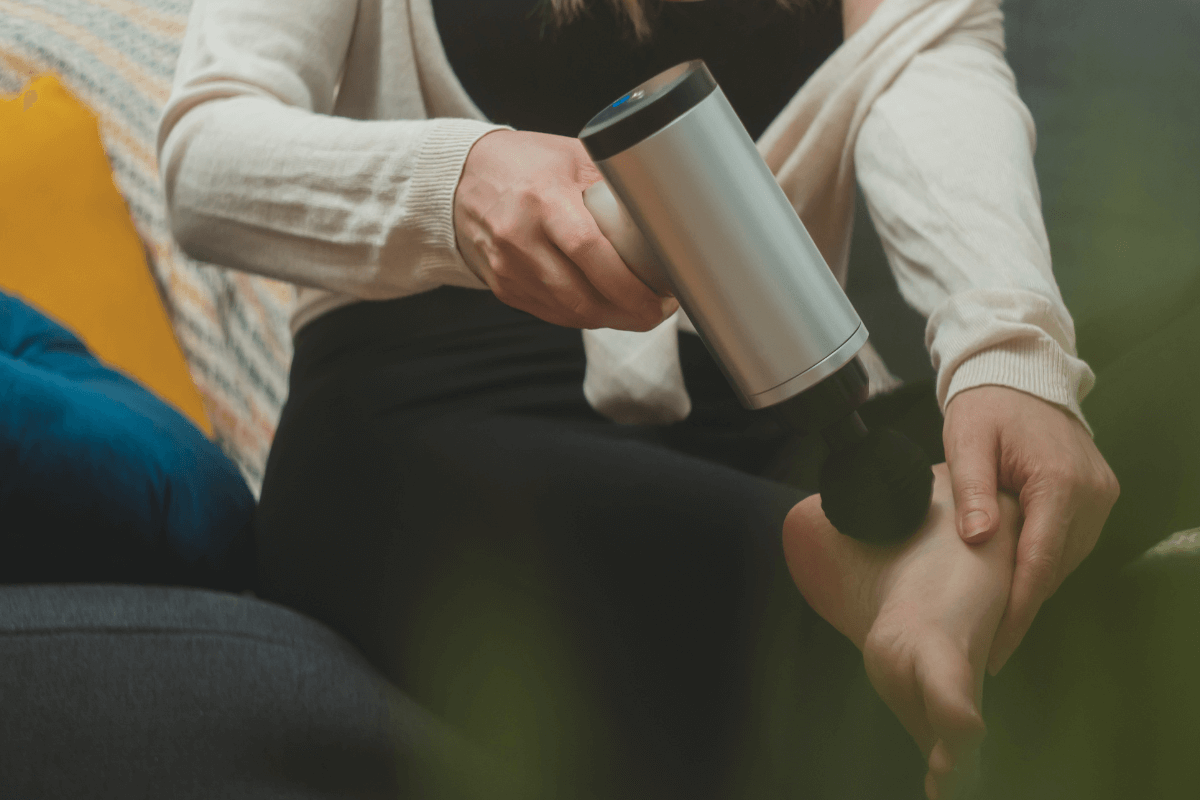 Técnica de massagem na planta do pé Pessoa sentada massageando a sola do pé com a pistola massageadora para relaxar a fáscia plantar e aliviar dores.