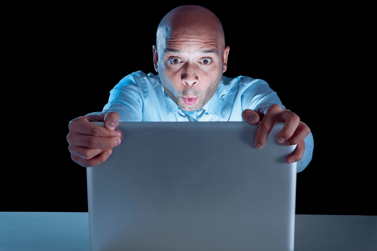 Homem segurando a tela do notebook com expressão de surpresa e excitação, ilustrando a descoberta sobre o que é um conteúdo adulto na internet.