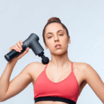 Mulher segurando uma pistola massageadora próxima ao ombro e pescoço, ilustrando o artigo sobre onde não se pode colocar o massageador elétrico para evitar lesões em áreas sensíveis e perigosas.