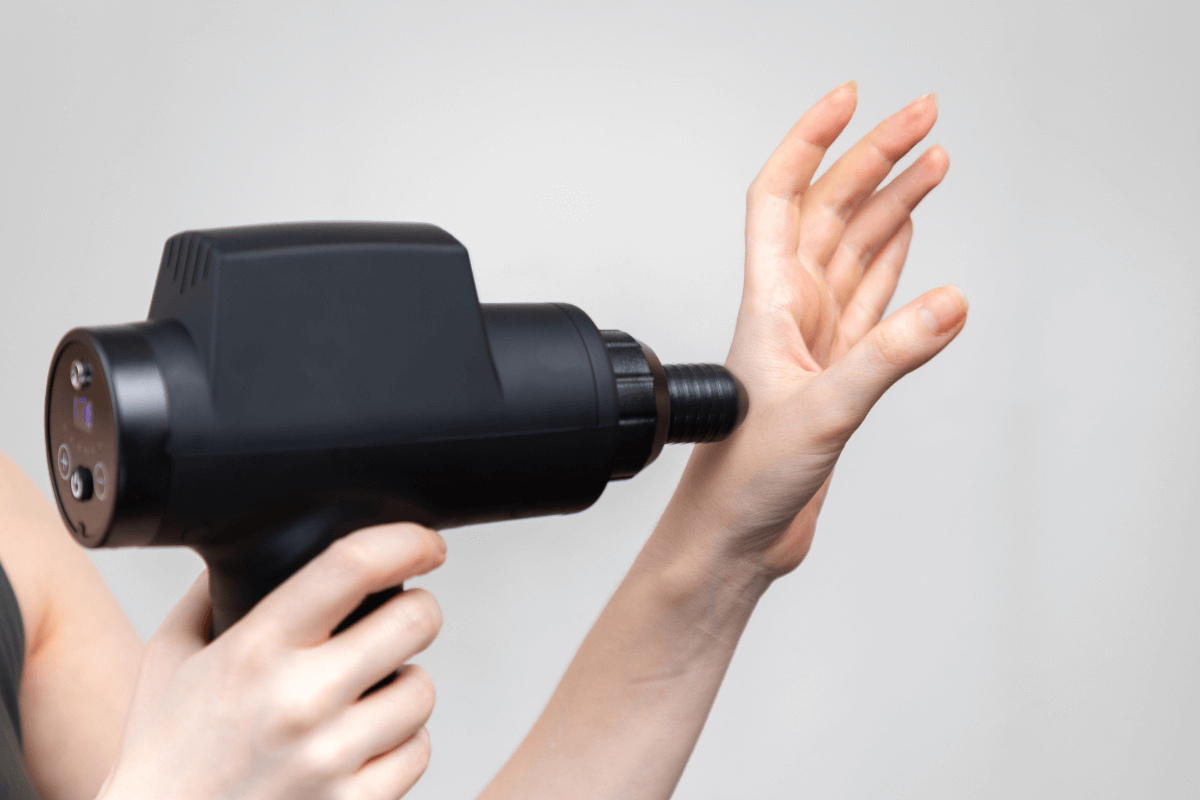 Estimulação da circulação na mão com terapia percussiva. Detalhe da pistola massageadora sendo aplicada na palma da mão para estimular a circulação sanguínea e aliviar a tensão nos tendões do punho.