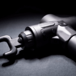 Close-up da pistola massageadora muscular profissional na cor preta com a ponteira garfo acoplada, ideal para relaxamento da coluna e alívio de tensão.