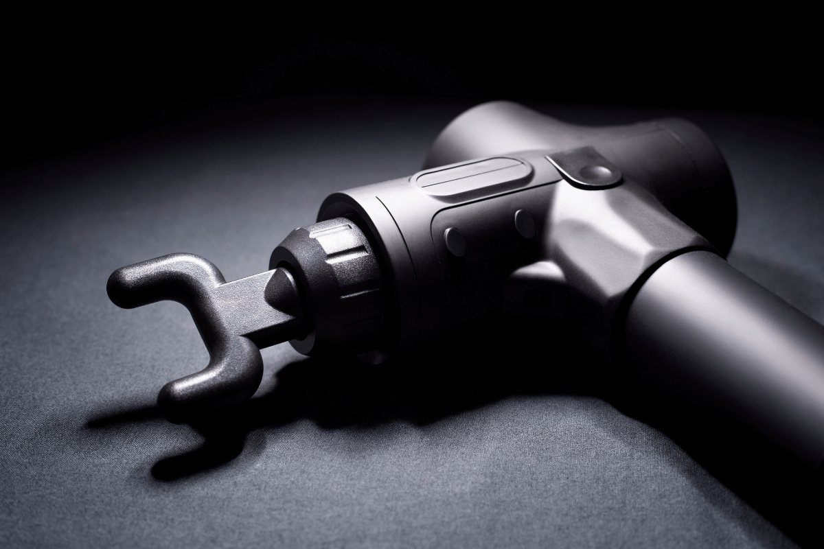 Close-up da pistola massageadora muscular profissional na cor preta com a ponteira garfo acoplada, ideal para relaxamento da coluna e alívio de tensão.