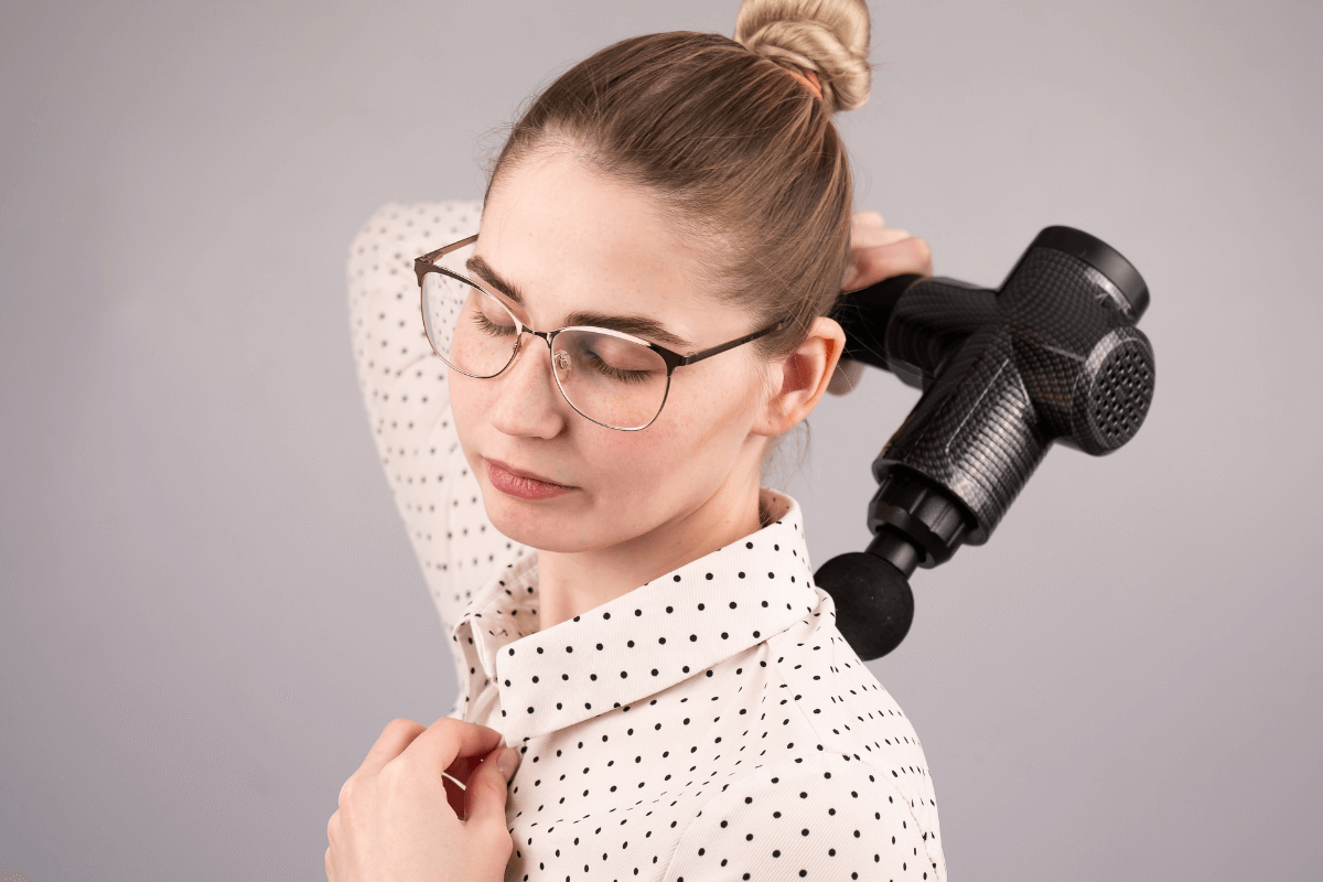 Ajuste de pressão: Deixe a vibração trabalhar pelo músculo Mulher aplicando a pistola massageadora no ombro com pressão suave e olhos fechados, demonstrando como deixar o peso do aparelho agir sem forçar o motor ou machucar a pele.
