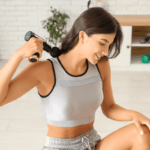 Mulher fitness sorrindo enquanto aplica a pistola massageadora no trapézio para aliviar a tensão e demonstrar na prática qual o benefício do relaxamento muscular imediato.