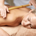 Mulher deitada recebendo massagem com hastes de bambu nas costas em clínica de estética, ilustrando o artigo sobre qual o valor de uma sessão de bambuterapia.