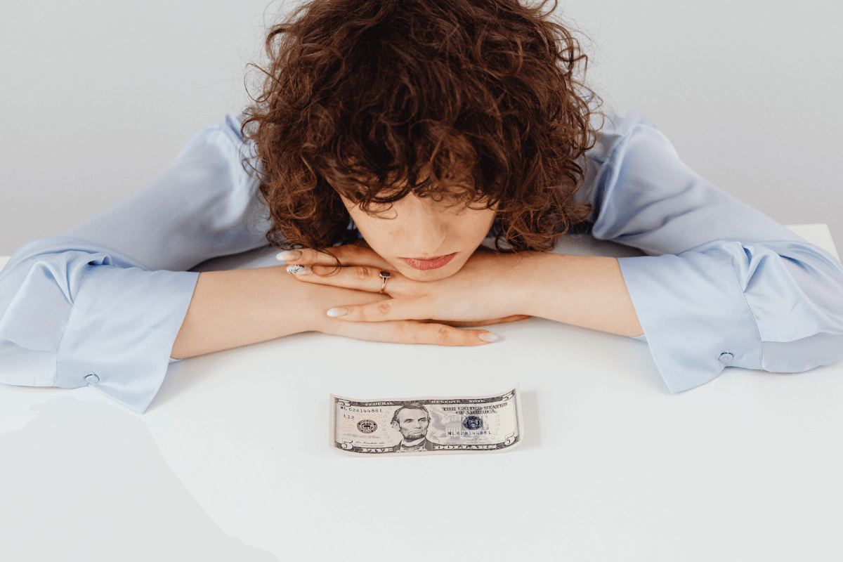 Mulher analisando nota de cinco dólares sobre a mesa, ilustrando o planejamento financeiro e a vantagem de receber em moeda forte ao vender conteúdo adulto.