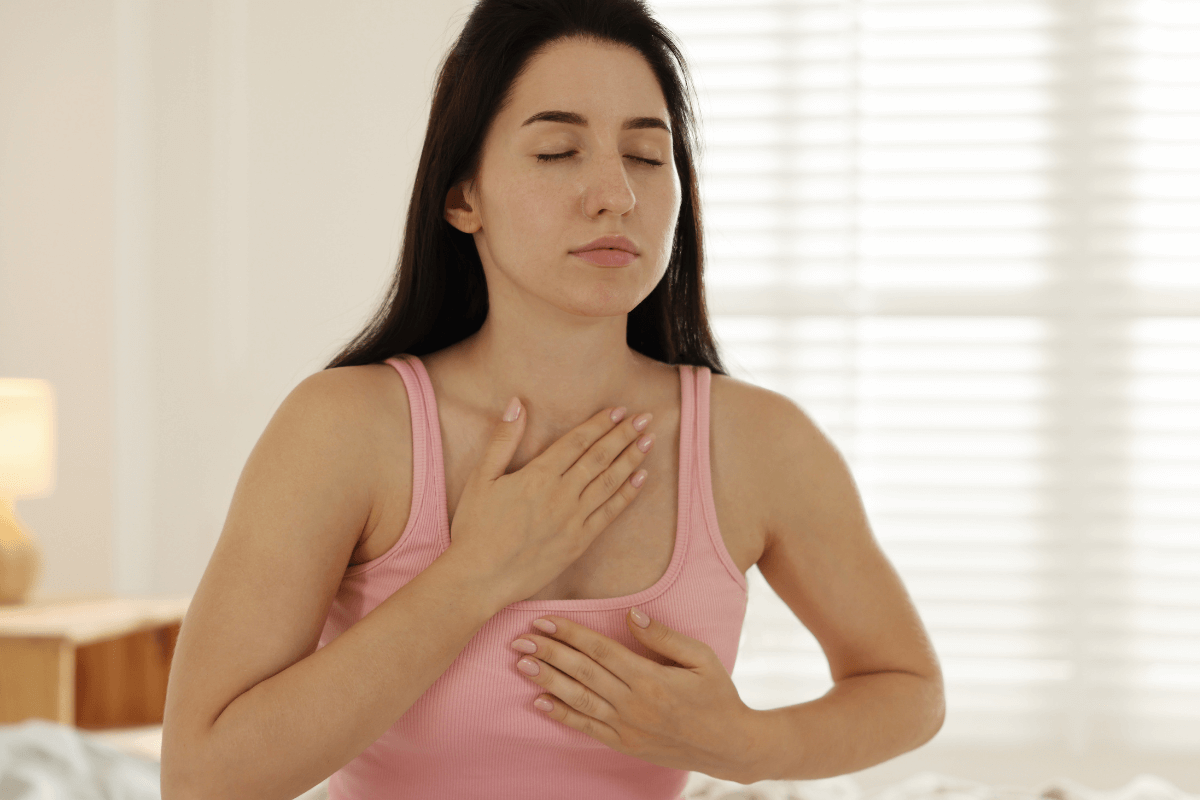 Mulher com as mãos no peito e abdômen praticando respiração profunda e consciente, ilustrando como relaxar a musculatura interna para potencializar o efeito de usar massageador na barriga.